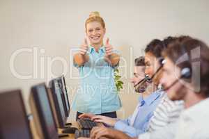 Businesswoman with thumbs up standing at employees