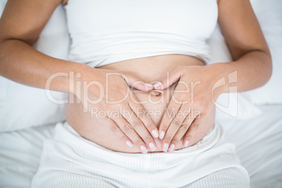 Close-up of pregnant woman doing heart sign on her belly