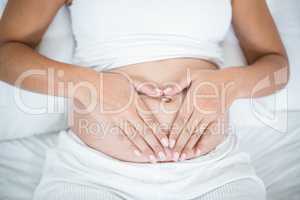 Close-up of pregnant woman doing heart sign on her belly