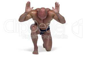 Muscular man bending on knee with arms raised
