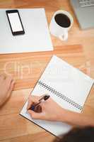 Man writing on spiral notebook at desk in office