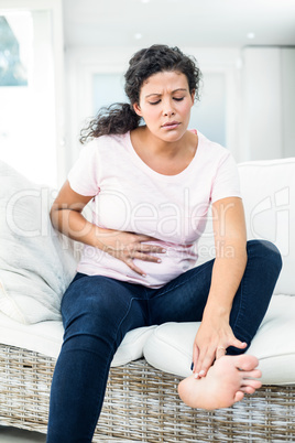 Pregnant woman touching feet while holding belly