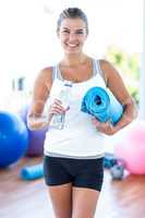 Smiling woman holding water bottle and yoga mat