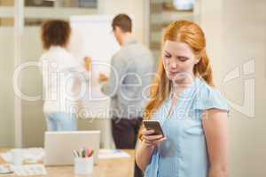 Businesswoman texting on phone with colleagues in background