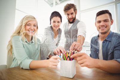 Portrait of smiling business people taking pencils from desk org