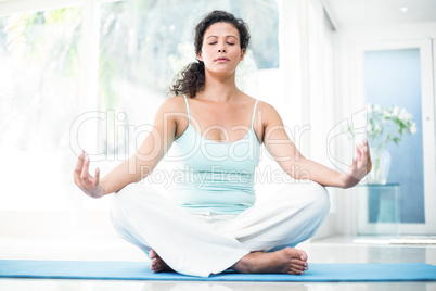 Pregnant woman doing yoga with eyes closed on exercise mat