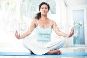 Pregnant woman doing yoga with eyes closed on exercise mat