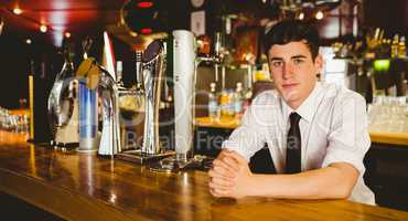 Confident male bartender sitting at bar counter