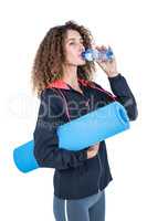 Young woman drinking water while holding exercise mat