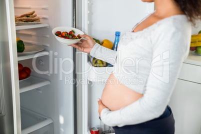 Pregnant woman keeping strawberries in fridge