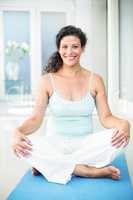 Portrait of happy pregnant woman sitting on exercise mat