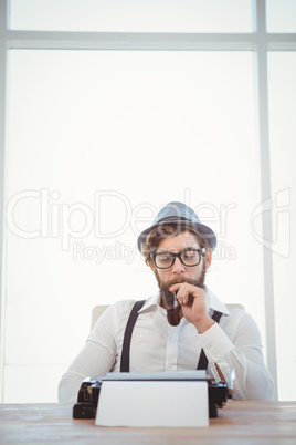 Hipster smoking pipe while sitting looking at typewriter