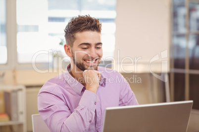 Businessman with hand on chin looking at laptop
