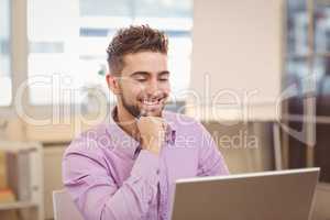 Businessman with hand on chin looking at laptop