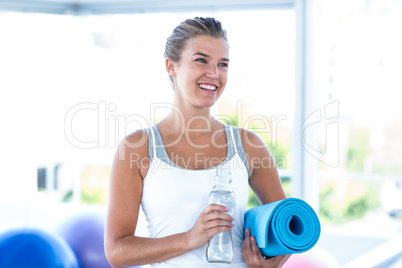 Beautiful woman smiling while holding water bottle and yoga mat