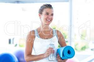 Beautiful woman smiling while holding water bottle and yoga mat