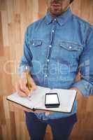 Mid section of man with mobile phone writing on book