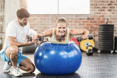 Male trainer helping young woman with the dumbbells