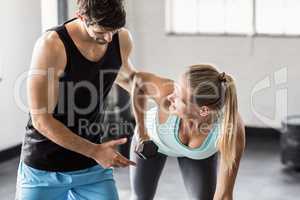 Male trainer helping young woman with dumbbells