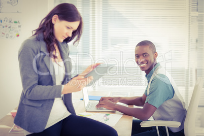 Portrait of smiling businessman working on laptop with woman usi