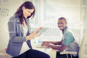 Portrait of smiling businessman working on laptop with woman usi