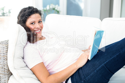 Happy pregnant woman with book on sofa