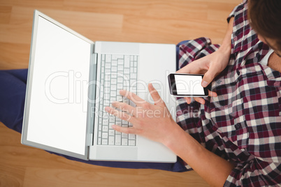 Hipster sitting with laptop using smartphone