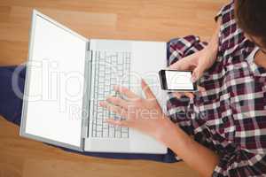 Hipster sitting with laptop using smartphone