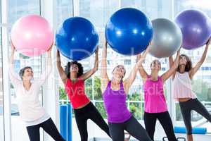 Women holding exercise balls with arms raised