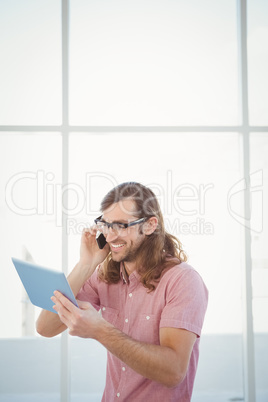 Hipster using mobile phone while looking at digital tablet