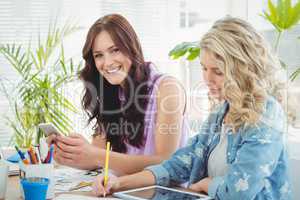 Portrait of smiling woman using smartphone while sitting at desk