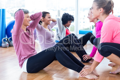 Women helping friends to do sit ups