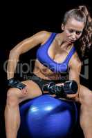 Thoughtful woman lifting dumbbell while sitting on exercise ball