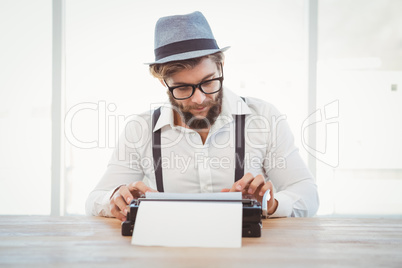 Hipster wearing eye glasses and hat working on typewriter