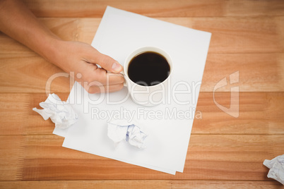 Man holding black coffee cup on paper at desk