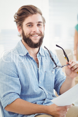 Portrait of smiling man holding eyeglasses and paper