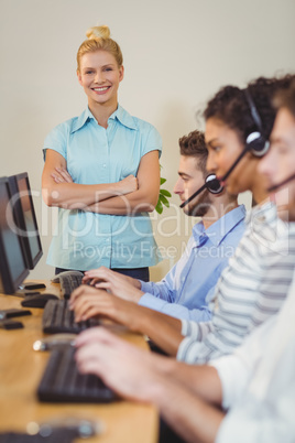 Happy businesswoman with arms crossed standing at employees