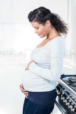 Pregnant woman touching her belly while standing in kitchen