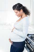 Pregnant woman touching her belly while standing in kitchen