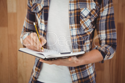 Mid section of hipster writing with pencil on book