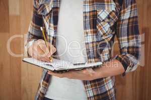 Mid section of hipster writing with pencil on book