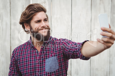 Hipster taking selfie against wooden wall