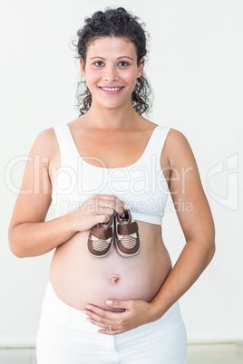 Smiling pregnant woman showing baby shoes