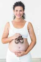 Smiling pregnant woman showing baby shoes