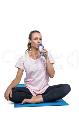 Sporty woman drinking water while sitting on mat