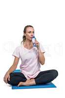 Sporty woman drinking water while sitting on mat