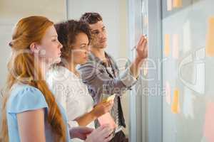 Businessman writing on glass as female colleagues looking at it