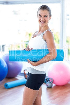 Side view of woman smiling while holding yoga mat
