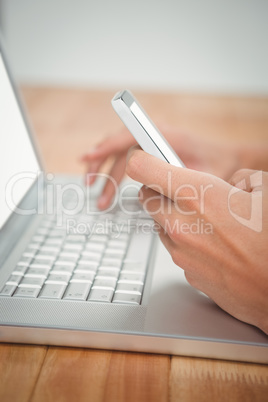Man using mobile phone while typing on laptop