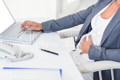 Pregnant businesswoman touching her belly while typing on laptop